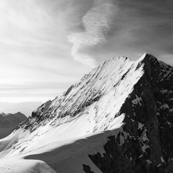 Photographie de montagne Alpes — la Barre des Écrins vue depuis le Dôme des Écrins, avec des silhouettes d’alpinistes minuscules sur les pentes, en noir et blanc, série Neige & Roche par Adelin Benard.